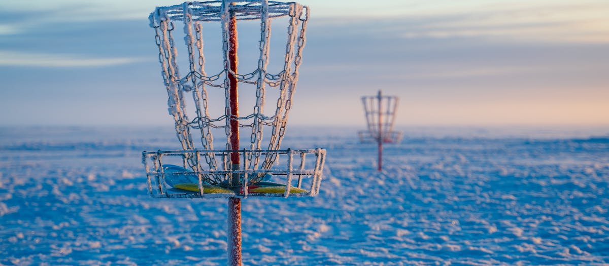 Frosty disc golf basket in a snowy open field during a winter sunrise, capturing serene outdoor vibes.