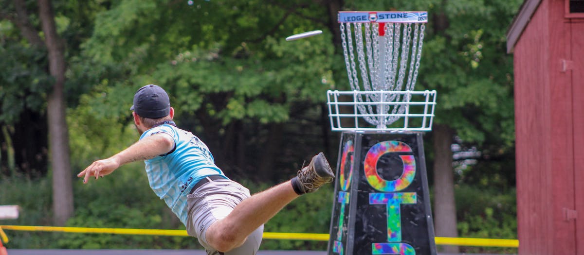 Man playing disc golf outdoors, expertly throwing frisbee towards basket in a lively game.